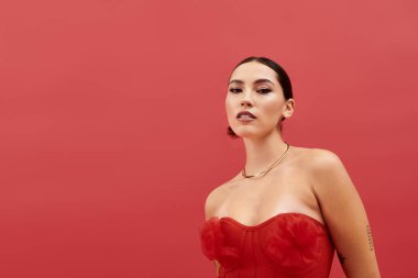 Güzel bir kadın kırmızı duvarın önünde dururken zarafet ve duruş sergiliyor..