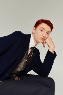 A young man with striking red hair showcases a fashionable layered outfit while posing creatively indoors. clipart