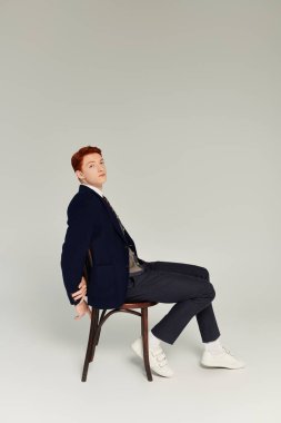 Kızıl saçlı genç bir adam şık kış kıyafetlerini sergiliyor, stüdyo ortamında kendine güveni tam..