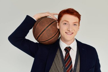 Kızıl saçlı kendine güvenen bir öğrenci elinde basketbol topuyla şık bir kış elbisesi içinde poz veriyor..