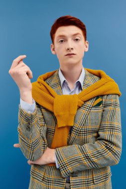 Çarpıcı kızıl saçlı genç bir adam şık kış kıyafetlerini rahat bir stüdyo ortamında sergiliyor..