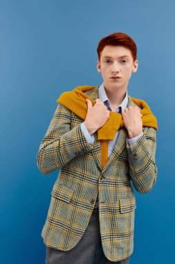 Genç bir adam, koyu mavi bir zemine karşı katmanlı kış kıyafetlerini sergiliyor..