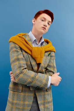 Kızıl saçlı şık bir genç adam katmanlı dokuları olan zarif bir kış elbisesi içinde güven içinde poz verir..