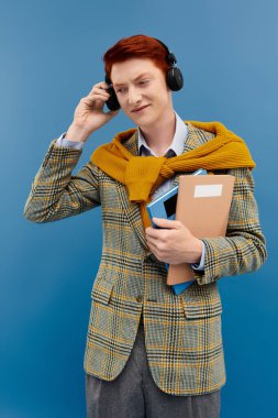 A young man with striking red hair wears a checkered blazer and a yellow sweater, immersed in music while studying. clipart