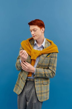 Canlı kızıl saçlı şık bir genç adam mavi bir ortama karşı şık bir kış elbisesi içinde güven içinde poz verir..