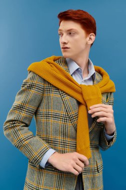Genç bir adam son moda bir kış kıyafeti sergiliyor, katmanlar ve bir stüdyoda renk patlaması var..