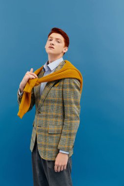 Çarpıcı kızıl saçlı genç bir adam katmanlı bir kıyafet giyer. Stüdyoda kendine güveni ve moda yeteneği yayar..