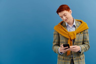 Katmanlı kış kıyafeti giyen şık adam, şık bir stüdyoda telefonuyla meşgul oluyor..