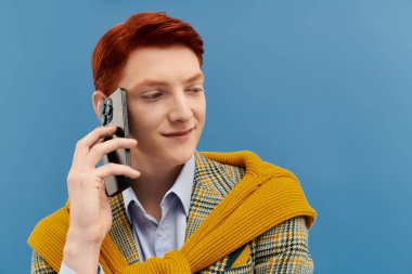 Modern bir stüdyoda, kızıl saçlı şık bir genç adam telefonla konuşurken gülümsüyor, kendine güveni tam..