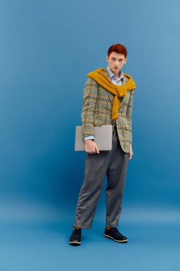 Kendine güvenen genç adam, mavi bir zemin karşısında canlı renklerle modaya uygun bir kış görüntüsü sergiliyor..