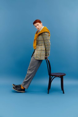 Katmanlı kış kıyafetleri giymiş zarif bir genç adam sandalyeye yaslanıyor, kendine güveni ve tarzı var..