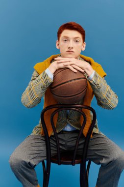 Kış kıyafetleri içinde şık bir genç adam basketbol topuyla oturur ve bir stüdyoya güveni tamdır..