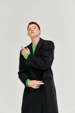 A confident young man with striking red hair showcases an elegant winter coat against a minimalist backdrop. clipart