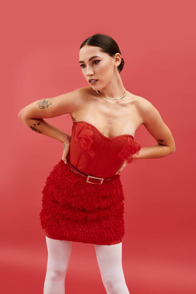 Молодая женщина позирует в потрясающем красном платье на ярком фоне.