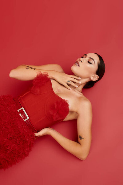 A stunning young woman showcases elegance in a striking red outfit while striking a pose.