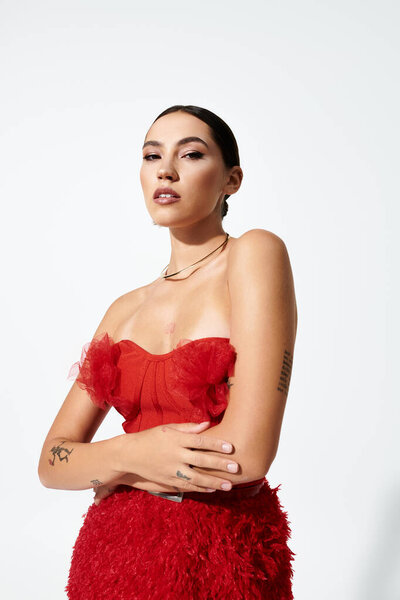 Поразительная молодая женщина демонстрирует смелое красное платье, принимая ее элегантность и обаяние в стиле.