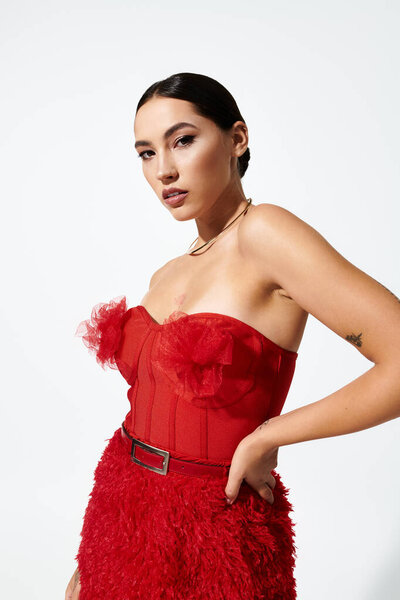 The young woman poses confidently in a striking red dress adorned with delicate ruffles.