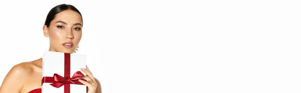 A young woman with an elegant pose showcases a gift wrapped in white paper and a red bow.