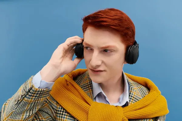 Kızıl saçlı yakışıklı genç bir adam parlak bir stüdyoda müzik dinlerken şık bir kış kıyafeti giyiyor..