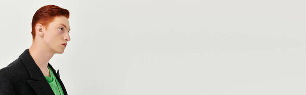 A young man with striking red hair models an elegant winter coat against a simple studio backdrop.