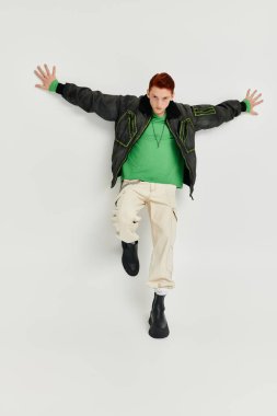 A young man with striking red hair elegantly poses in a winter coat within a bright studio environment. clipart