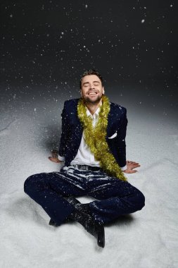 Genç bir adam, yumuşak bir karla oturmuş neşeli bir gülümsemeyle, şenlikli süslerle süslenmiş..