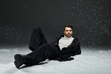 Yakışıklı genç bir adam karlı bir ortamda huzur içinde uzanıyor, modern kış kıyafetlerini sergiliyor..