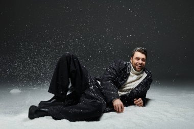 Neşeli genç bir adam karda yatıyor, kışın soğuğunu kucaklıyor ve gülümsüyor..