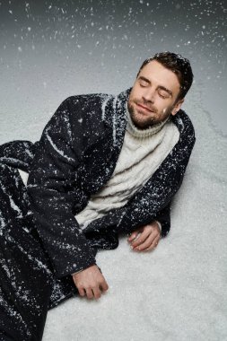 A handsome young man relaxes in soft, falling snow, embracing the winter seasons beauty.