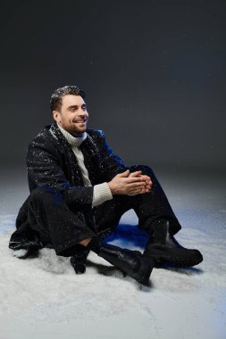 Karlı elbiseli genç adam sevinç içinde oturuyor, kış havasını ve neşeli ruhu kucaklıyor..