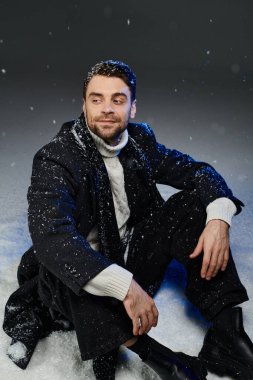 Kışın giyinmiş genç bir adam kar altında gülümser. Etrafı kar taneleriyle çevrilidir..