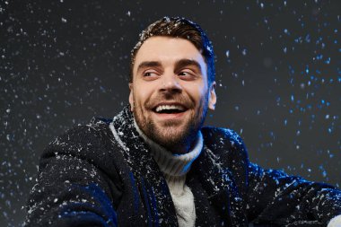 A cheerful young man shares a bright smile as snowflakes dance around him in a winter celebration. clipart