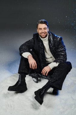 Yakışıklı genç bir adam karlı bir yüzeyde oturuyor, kışın sıcaklık ve neşe saçıyor..