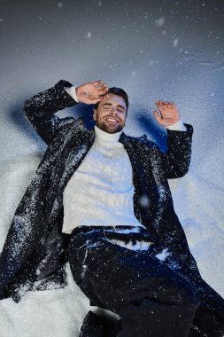 Yakışıklı bir adam kışın etrafı karla çevriliyken neşeyle gülümser..