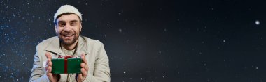 Rahat kıyafetli gülümseyen genç adam kış atmosferinin tadını çıkarırken bir hediye tutuyor.