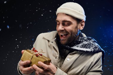 Genç bir adam, güzel paketlenmiş bir hediyeyi karın içinde tutarken neşeyle ışıldıyor..