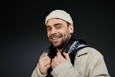 A stylish young man radiates positivity while adjusting his scarf with a bright smile.