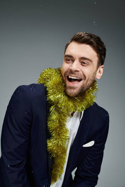 A dapper young man in a suit joyfully shows off a playful expression with festive garland.