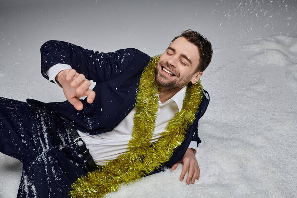 Радостный молодой человек смеется, лежа в снегу, украшенный веселыми праздничными украшениями вокруг него.