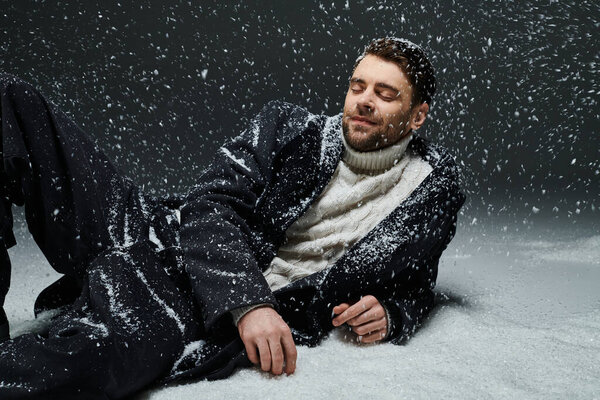 A dashing young man relaxes gracefully in a snowy environment with a peaceful expression.
