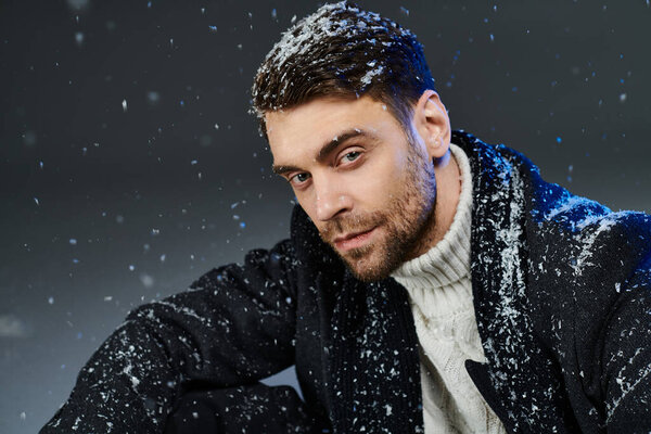 The striking young man is captured playfully in falling snowflakes while staying warm.