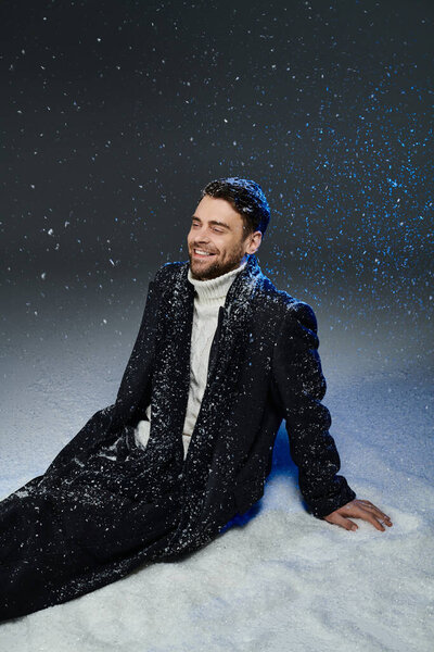 A handsome young man smiles brightly as snowflakes cascade around him, creating a joyful atmosphere.