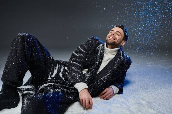 A young man plays in the snow, smiling in his stylish winter outfit.