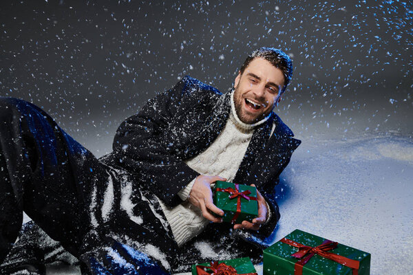 Веселый молодой человек любит играть в снегу с зелеными завернутыми подарками вокруг него.