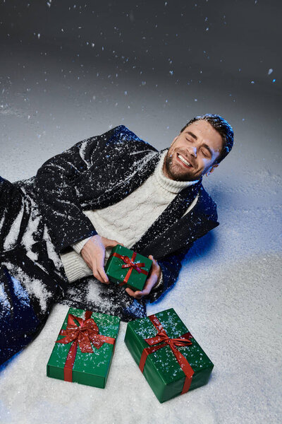A handsome young man smiles while surrounded by festive gift boxes in the snow.