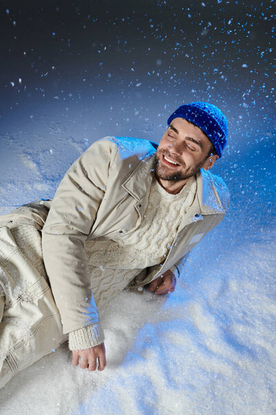 Молодой человек смеется, расслабляясь в снегу, окруженный атмосферой зимней страны чудес.