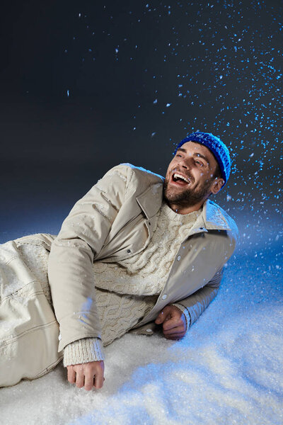 A young man dressed warmly smiles brightly as snowflakes dance around him in winter.