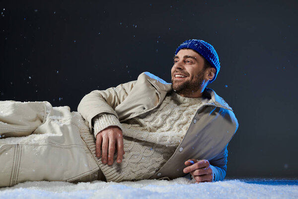 Веселый молодой человек расслабляется в снегу, улыбаясь, как снежинки мягко падают вокруг него.