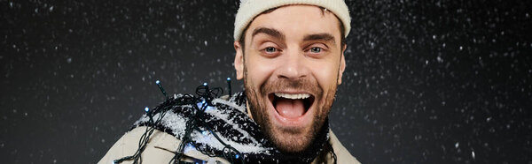 A happy young man with a big smile enjoys a snowy winter day adorned with colorful lights