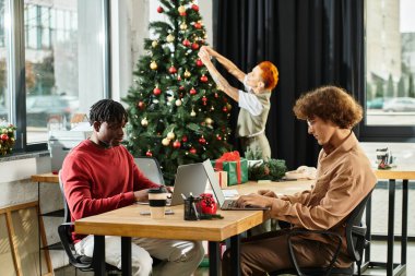 Meslektaşlar ofis ağacını süslerken ve gülümsemelerini paylaşırken tatil ruhunun tadını çıkarırlar..